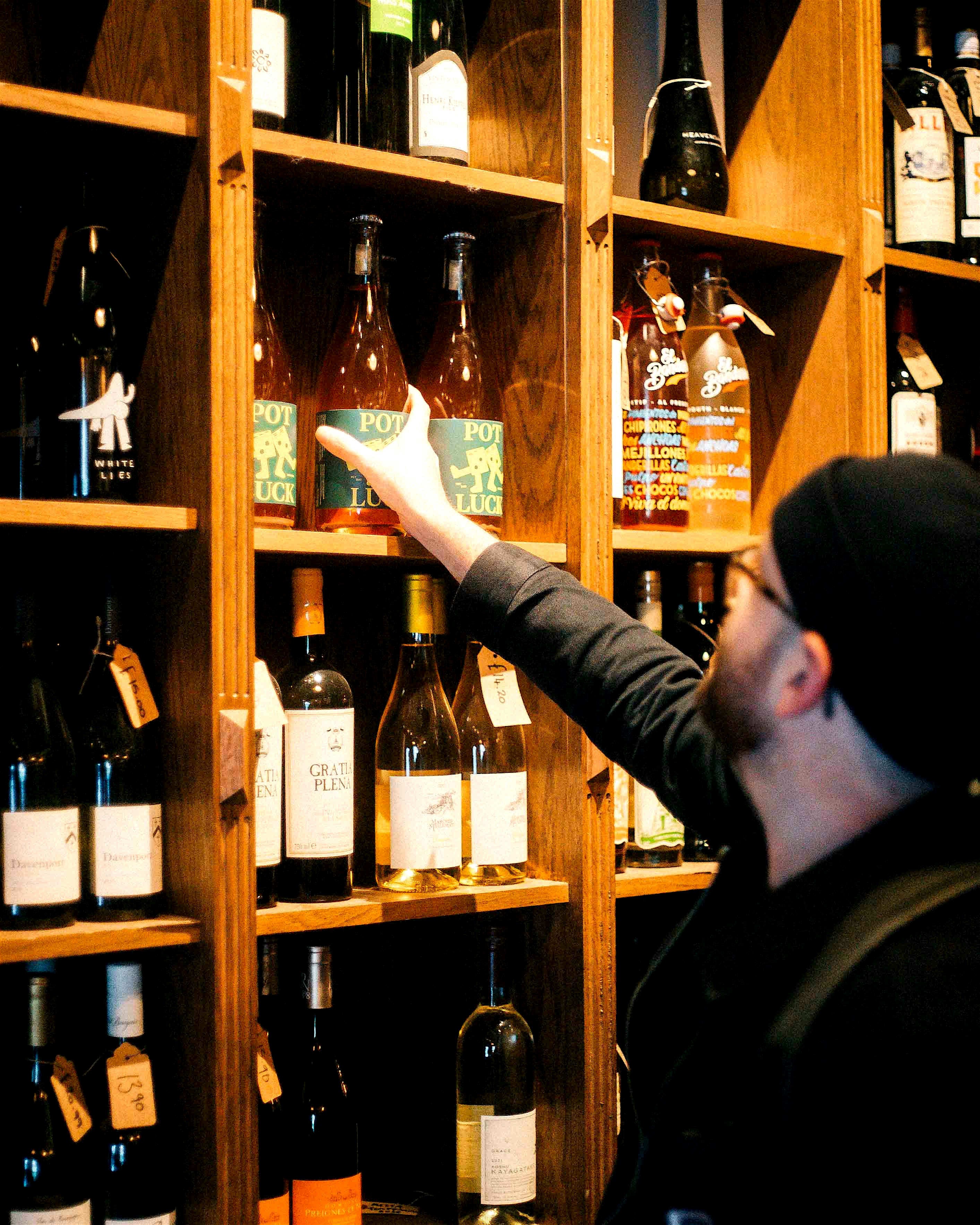 Man reaches on a high shelf for a bottle of wine in Shoreditch